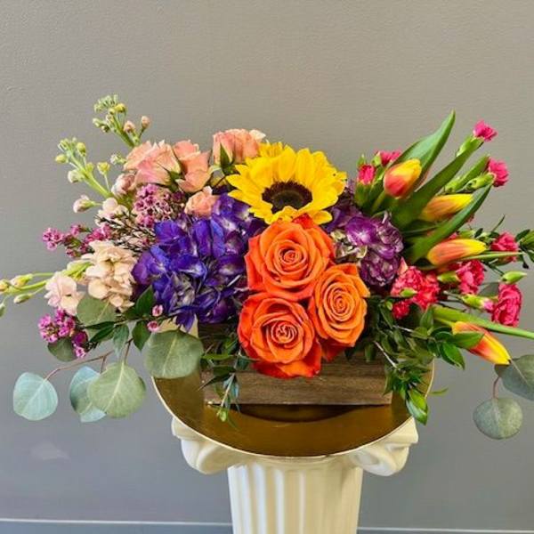 Colorful mixed flower arrangement in a wooden box on a pedestal