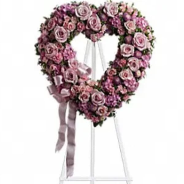 Heart-shaped pink rose wreath on a white stand with ribbon