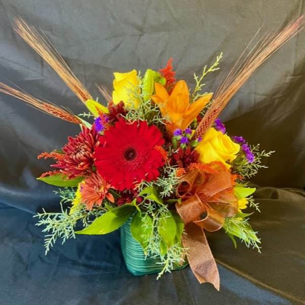 Bright mixed bouquet in a teal vase with a brown ribbon