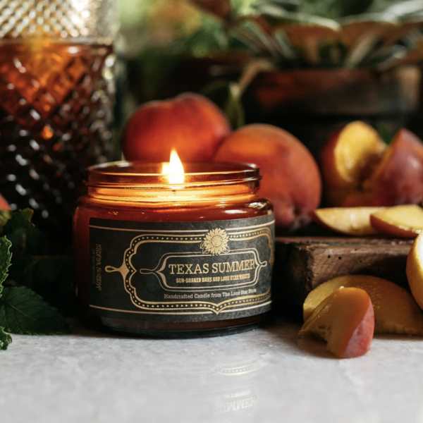 Lit candle in a glass jar surrounded by peaches and fruit slices