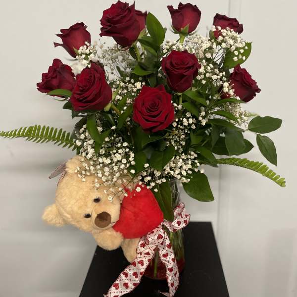 Bouquet of red roses in a glass vase with a teddy bear and heart ribbon