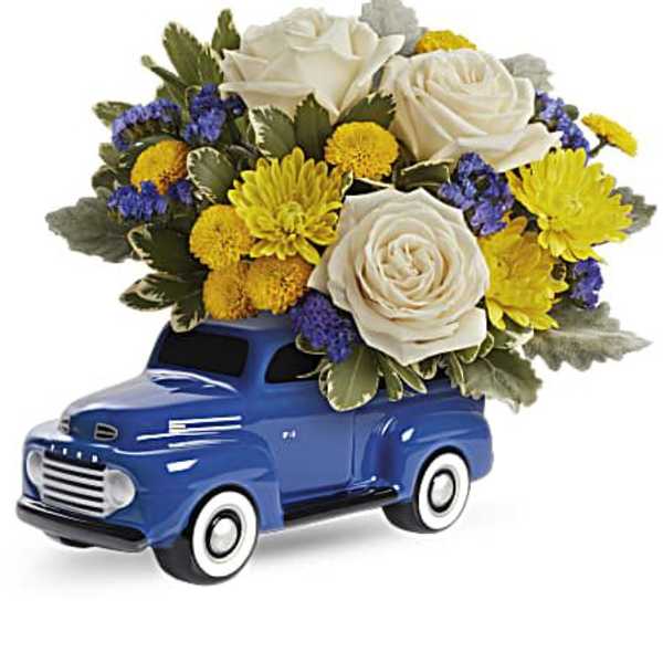 Blue toy truck topped with white roses and yellow flowers