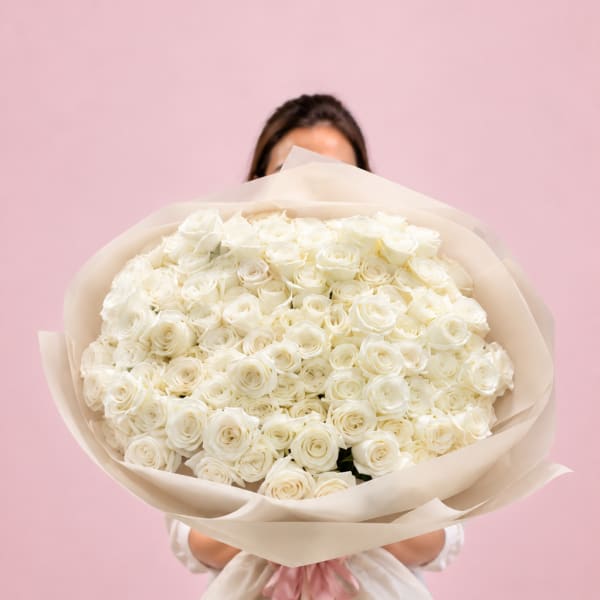 Large bouquet of white roses wrapped in cream paper with a pink ribbon
