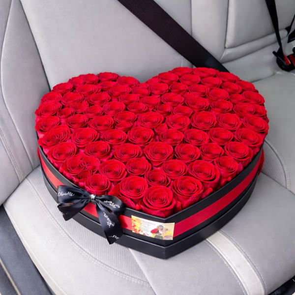 Heart-shaped box filled with red roses and tied with a black ribbon