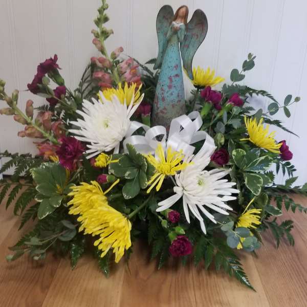 Low floral arrangement with yellow and white chrysanthemums and a winged angel figurine