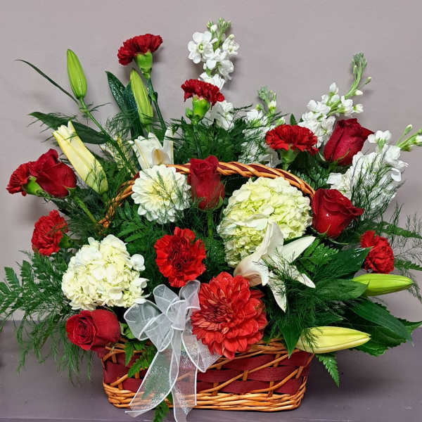 Basket arrangement of red roses, carnations, lilies, and white blooms with a ribbon bow