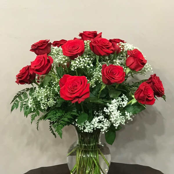 Red roses arranged in a clear glass vase with white filler flowers
