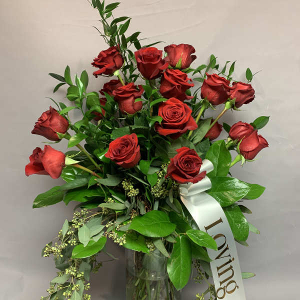 Red roses arranged in a clear glass vase with a white ribbon.