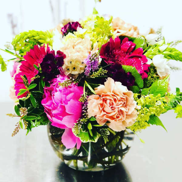 Bright mixed bouquet in a clear glass vase with pink, peach, white, and green blooms.