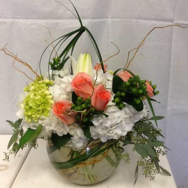 Arrangement of pink roses, white hydrangeas, and a lily in a glass bowl