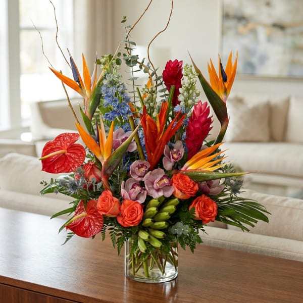 Tropical flower arrangement in a glass vase with orange bird-of-paradise and red blooms