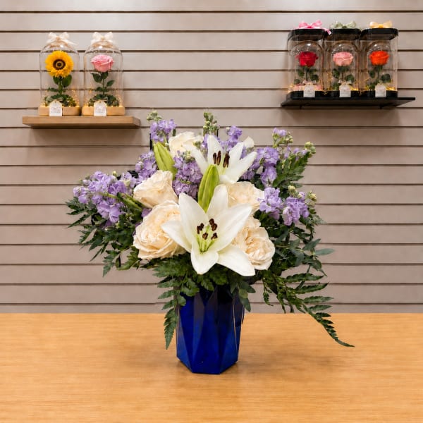 Bouquet of white lilies, cream roses, and purple flowers in a blue vase