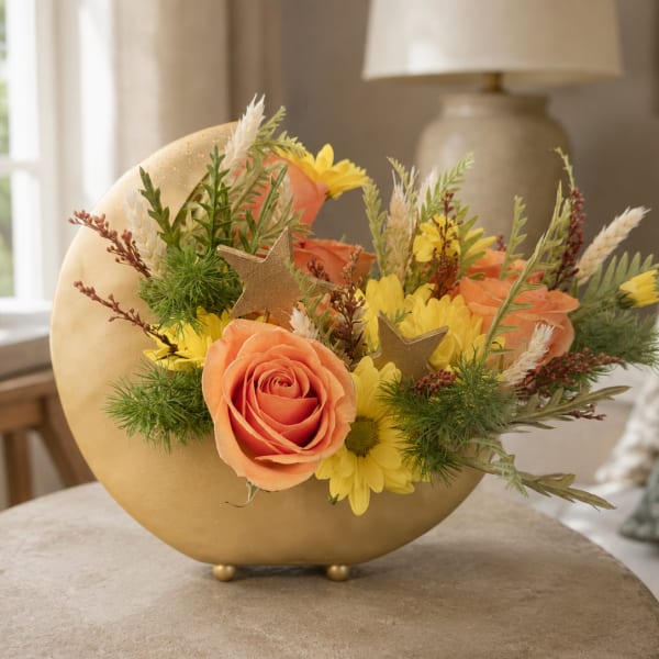 Peach roses and yellow daisies arranged in a gold crescent vase