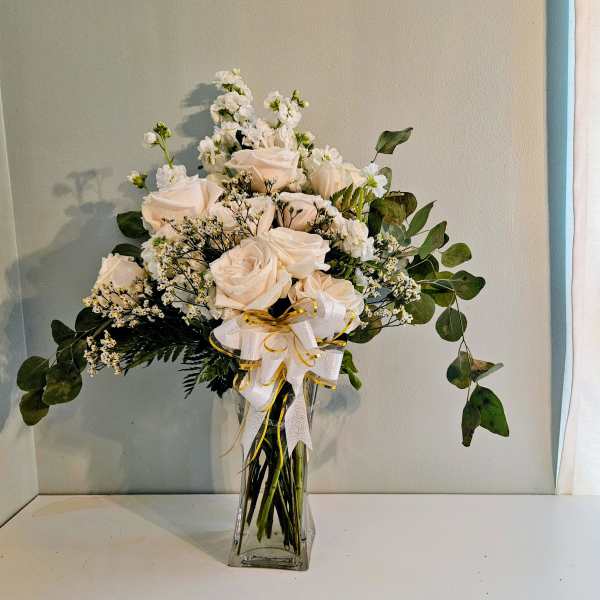 White roses and small white flowers in a clear glass vase with a ribbon