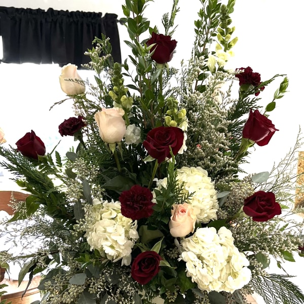 Tall arrangement of red and blush roses with white hydrangeas in a vase