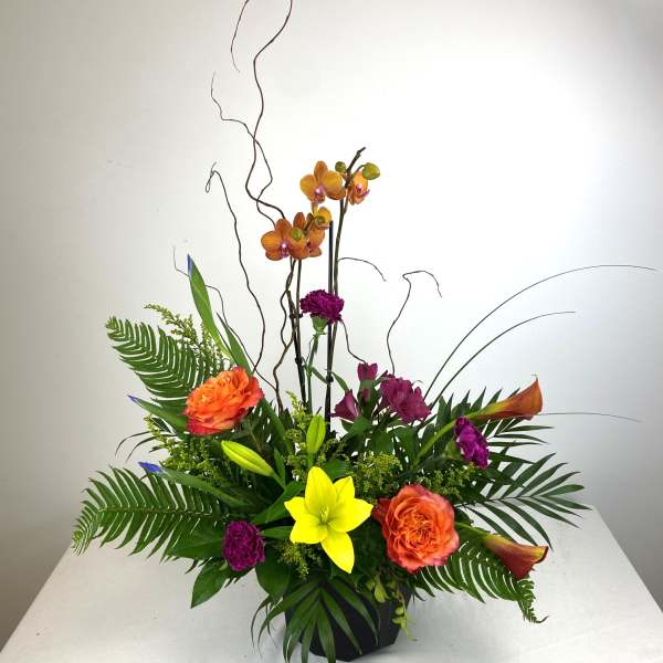 Tropical flower arrangement with orchids, lilies, and orange roses in a black vase