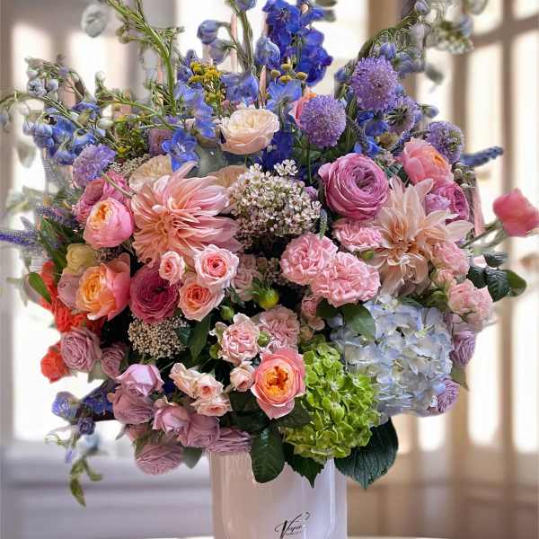 Large pastel bouquet in a white vase with pink, blue, and purple flowers