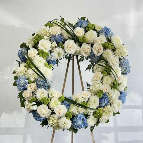Large floral wreath on a wooden easel with white, blue, and green blooms