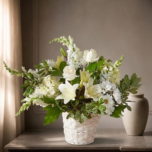 White floral arrangement in a woven basket with lilies, roses, and daisies