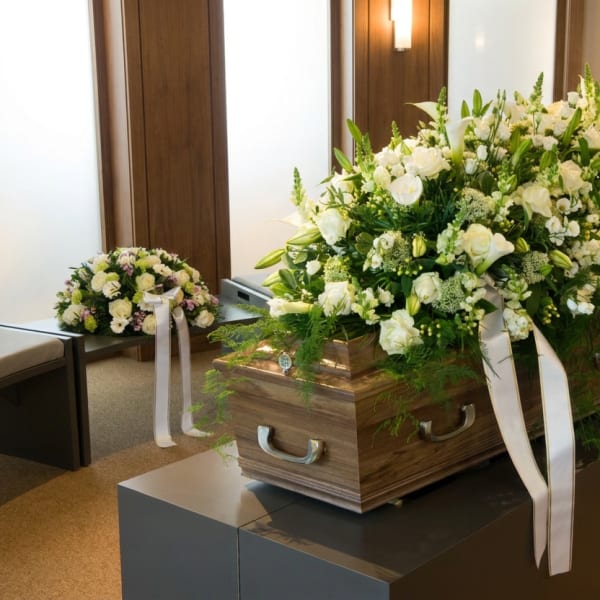 White floral casket spray on a wooden casket with a matching smaller arrangement nearby.