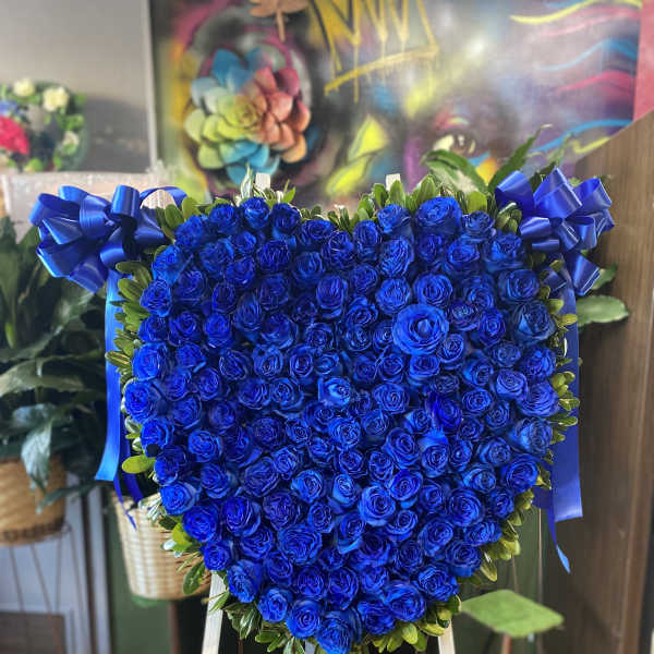 Heart-shaped arrangement of blue roses with ribbon bows on an easel
