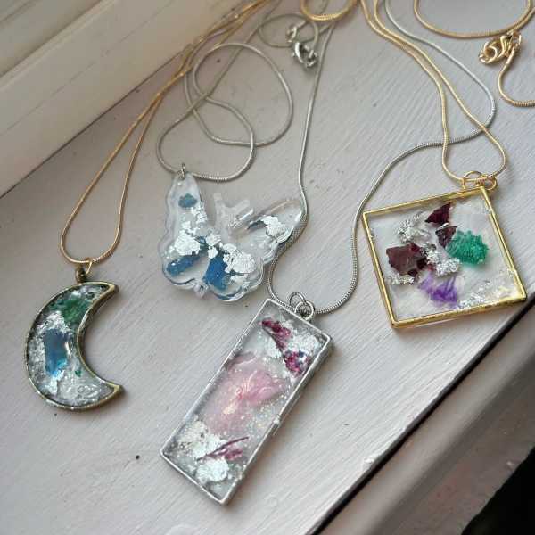 Four resin pendants on chains with dried flower and foil inlays