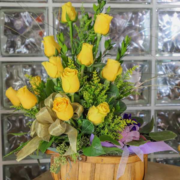 Yellow roses arranged in a wooden basket with ribbon accents