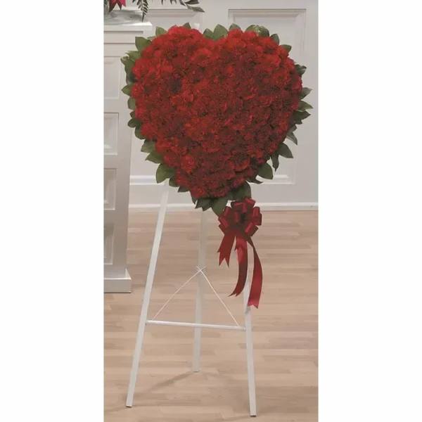 Heart-shaped red floral standing spray on a white easel with ribbon