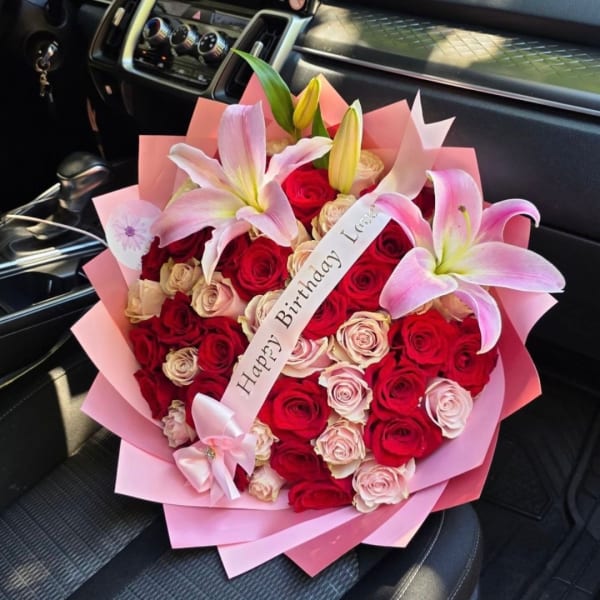 Bouquet of red and blush roses with pink lilies and a birthday ribbon