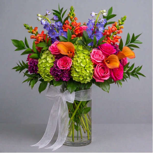 Bright mixed bouquet with pink roses, orange calla lilies, and purple blooms in a glass vase
