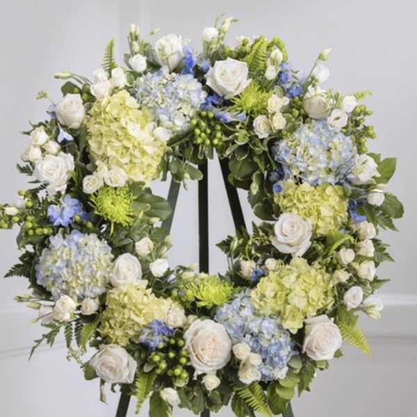 Floral wreath with white roses, blue hydrangeas, and pale green blooms on an easel