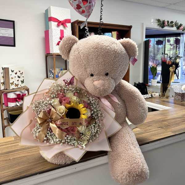 Teddy bear holding a pink bouquet with heart balloons above