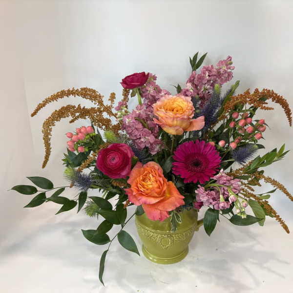 Mixed bouquet of roses, gerbera daisies, and pink blooms in a green vase