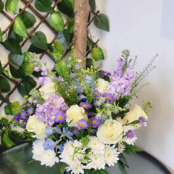 Mixed bouquet of white roses, purple flowers, and white daisies in a blue vase