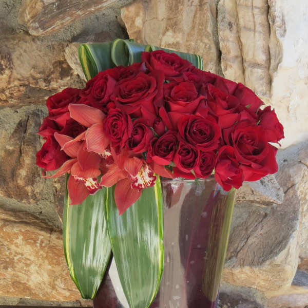 Red roses and coral orchids arranged in a glass vase