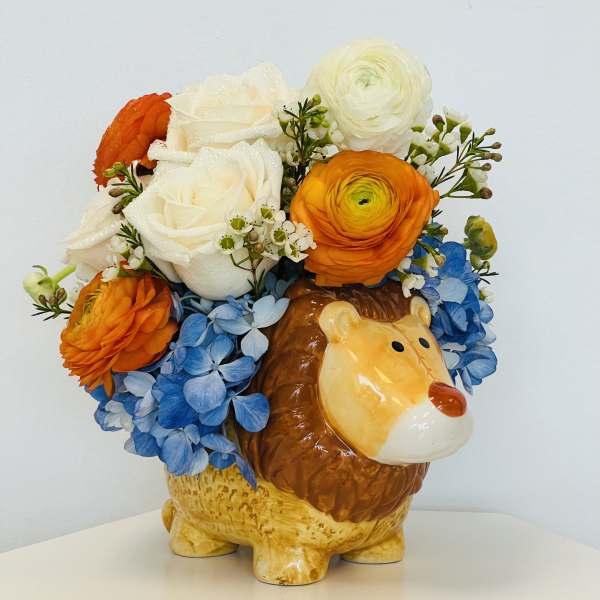 Flower arrangement in a ceramic lion planter with blue hydrangeas and orange and white blooms