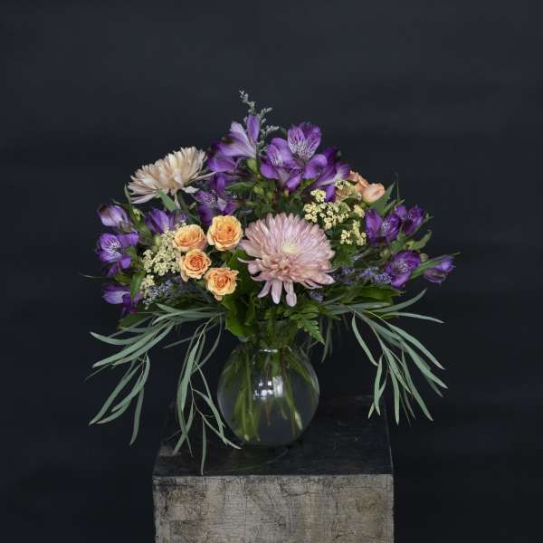 Mixed bouquet of purple, peach, and pink flowers in a glass vase