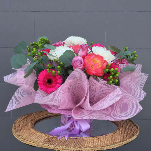 Pink and white mixed bouquet wrapped in pink paper with a purple ribbon