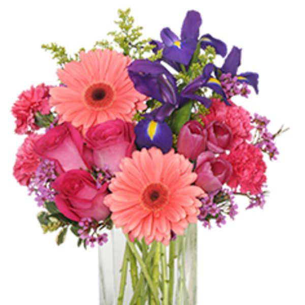 Pink gerberas, roses, carnations, and purple irises in a clear glass vase