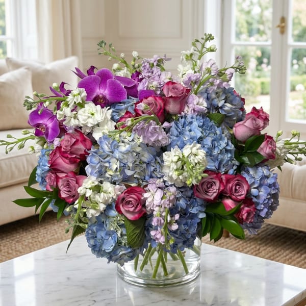 Bouquet of blue hydrangeas, pink roses, and purple orchids in a glass vase