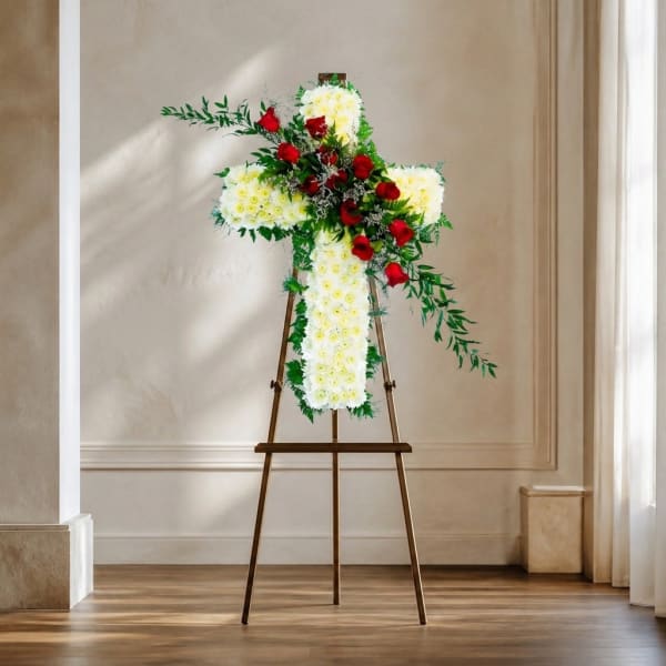 Cross-shaped floral tribute on an easel with white flowers and red roses