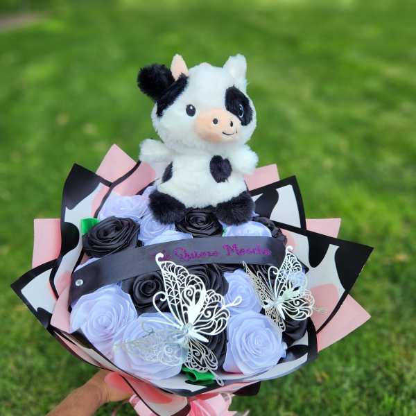 Plush cow atop a bouquet of black and lavender roses with butterfly decorations