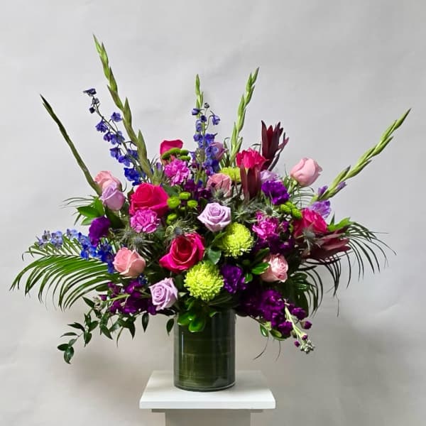 Tall mixed bouquet of roses, purple blooms, and green spikes in a glass vase