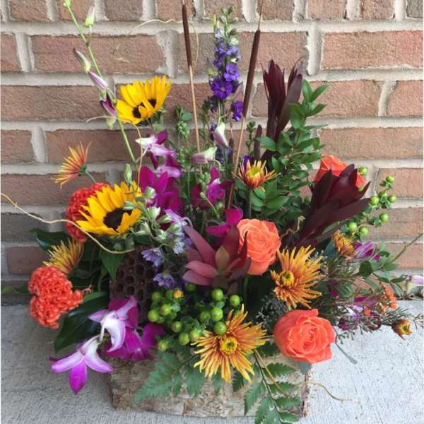 Mixed bouquet with sunflowers, roses, and purple blooms in a stone container