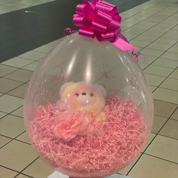 Clear balloon gift with a teddy bear and pink filler, topped with a magenta bow