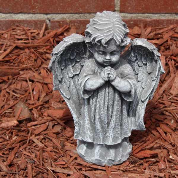 Stone angel statue with folded hands in a mulch bed