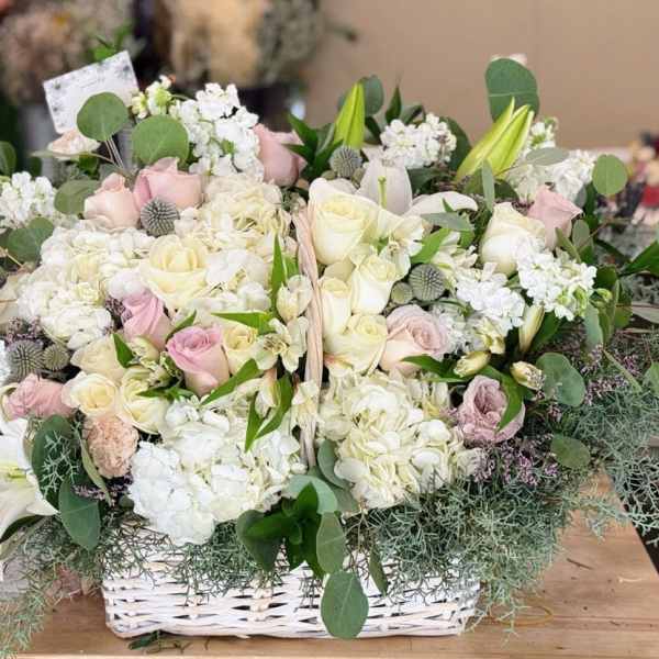 Basket arrangement of white and blush roses with lilies and greenery
