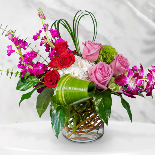 Pink and red roses with purple orchids in a glass vase