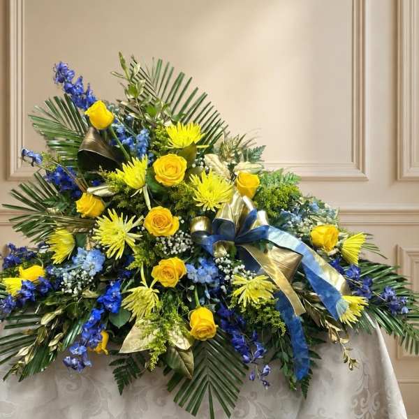 Large floral spray with yellow roses, blue flowers, and palm fronds