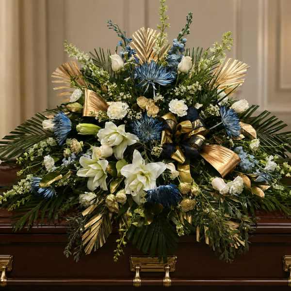 Large floral casket spray with white and blue flowers and gold ribbon accents